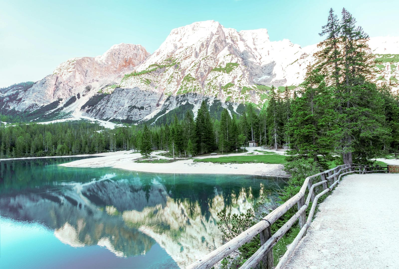 Stunning view of an alpine lake with clear reflections of snow-capped mountains and lush green trees.